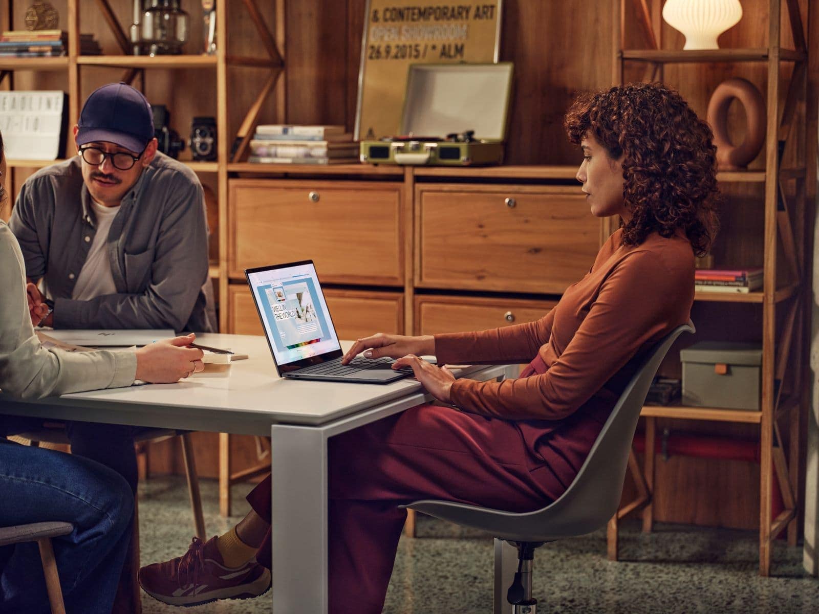 Diverse team collaborating in a creative office space with a woman using an HP laptop and a man in a cap, surrounded by bookshelves and art posters